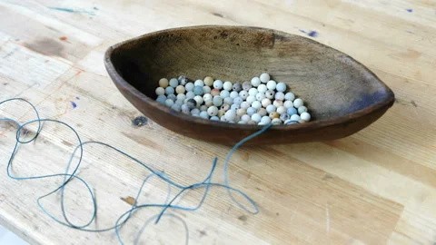 Weaving of beads. Closeup blue beads in a wooden bowl shaped like a boat on a Stock Footage 87585558