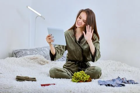 Web conference using tablet PC by happy woman who sits on bed indoors. Stock Photos