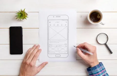 The web designer sketches the user interface on the wireframe of the mobile p Stock Photos