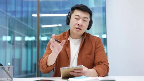 Webcam view. Asian businessman in wireless headphones watching video call Stock Footage 291541666