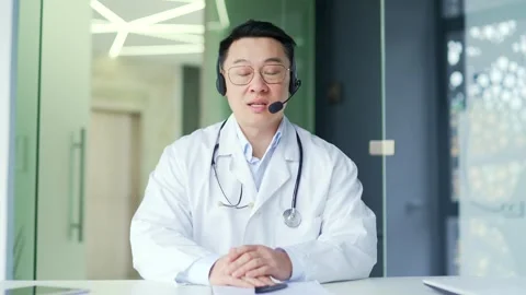 Webcam view. Asian doctor in headset tal... | Stock Video