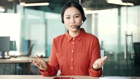 Webcam view. Asian female manager in wireless headset talking on video call Stock Footage 273099084