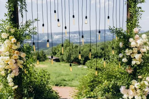 Wedding arch on rustuc style with white flowers in park with light bulbs. Stock Photos