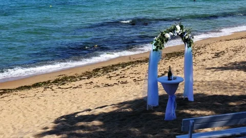 Wedding arch on sandy seaside with bench, flowers, and champagne table Stock Footage 318399682
