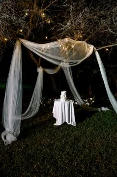 Wedding cake display under draped fabric and fairy lights at night Stock Photos