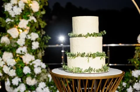 Wedding cake on the table against the background of an arch with flowers Stock Photos