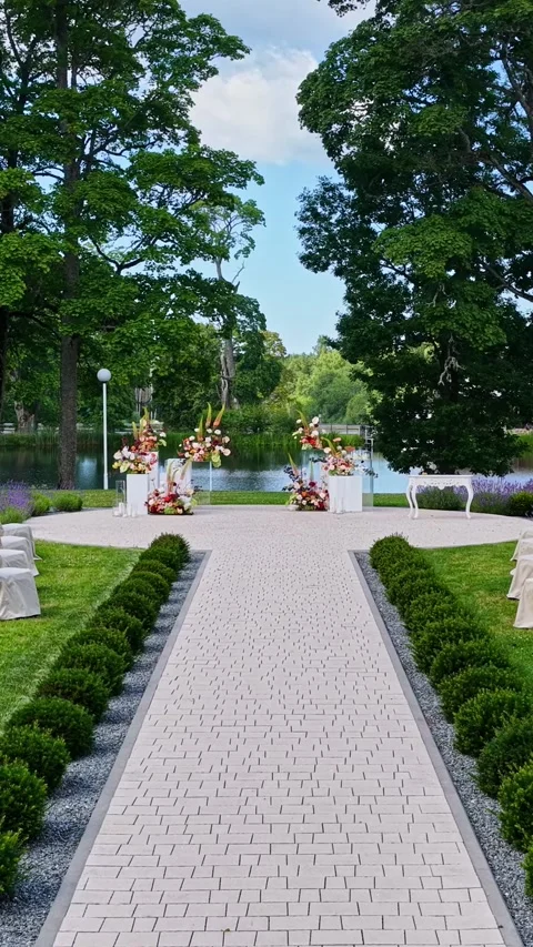 Wedding ceremony venue setup on paved walkway by lake with floral decorations 库存影片 348900073