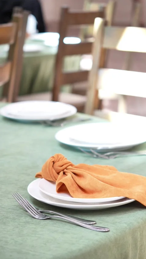 Wedding decorator placing orange and green wedding cloth napkins on plates on we Stock Footage 318558164