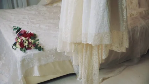 Wedding dress on hanger over bed with flower bouquet in bedroom Stock Footage