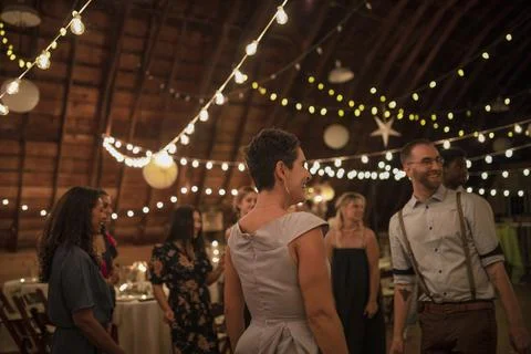 Wedding guests talking under string lights at wedding reception Stock Photos