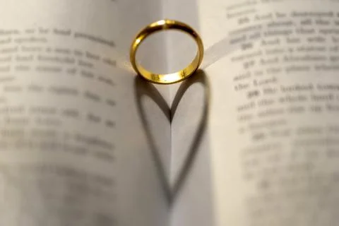 A wedding Ring on the bible with shadow of heart shape on the page Stock Photos