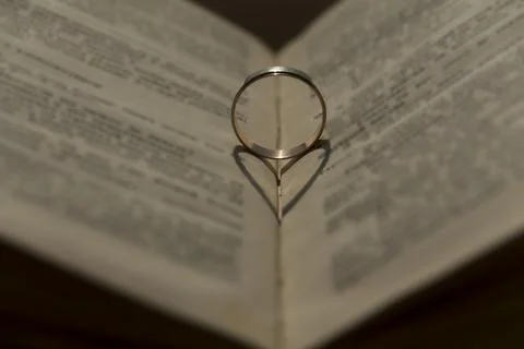 Wedding ring with a falling shadow in the form of a heart standing on an open Stock Photos