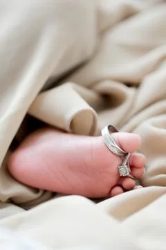 A wedding ring put on a small newborn baby feet Stock Photos