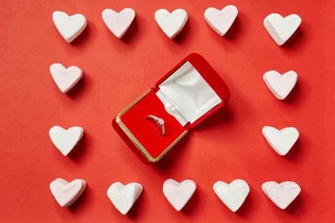 Wedding ring in a red box on a red background, white hearts are laid out around  Stock Photos