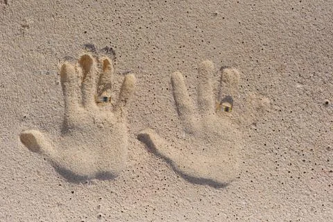 Wedding rings between handprints pressed into golden beach sand Stock Photos
