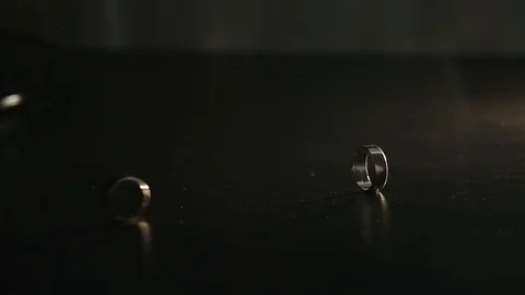 Wedding rings on black mirrored surface shining with light and rolling together. Stock Footage 120154694