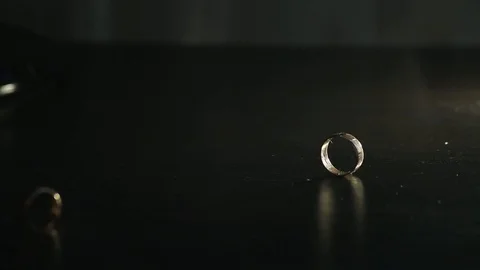 Wedding rings on black mirrored surface shining with light and rolling together. Stock Footage 120154768