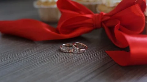 Wedding rings lie on the table. The camera moves smoothly. Red ribbons decorate  動画素材 98854658