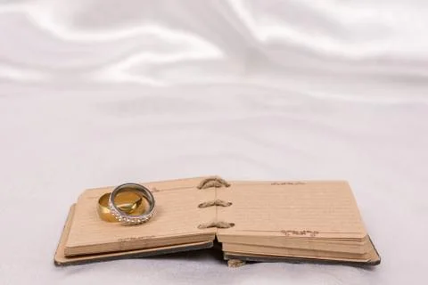 Wedding rings on rustic note paper over white satin Stock Photos