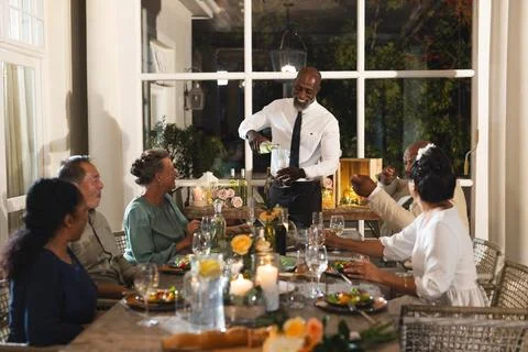At wedding, Server pouring wine for group of seniors enjoying dinner party at Foto stock