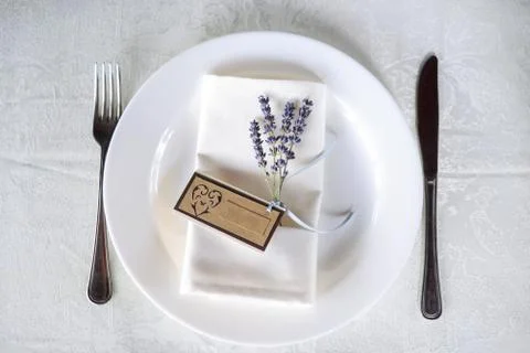 Wedding table setting with a plate, spoon, fork and a sprig of lilac with a sign Stock Photos
