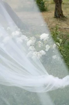Wedding veil draped over grass with white flowers in background Stock Photos