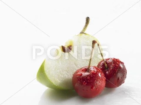 Wedge of green apple and two cherries with drops of water Stock Photos