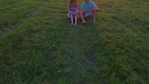 Weekend start. Young couple sit and fall back on green summer grass aerial Stock Footage 70997387
