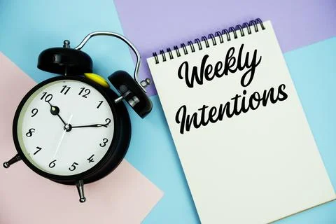 Weekly Intentions text written on notepad with alarm clock flat lay on mult.. Stock Photos
