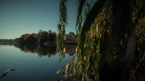 Weeping willow branches framing idyllic castle on lake during autumn Stock Footage 292787941