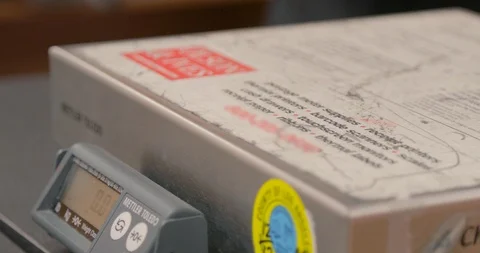 Weighing a package on a scale. Postal worker sets a box on a scale to get Stock Footage 97444599