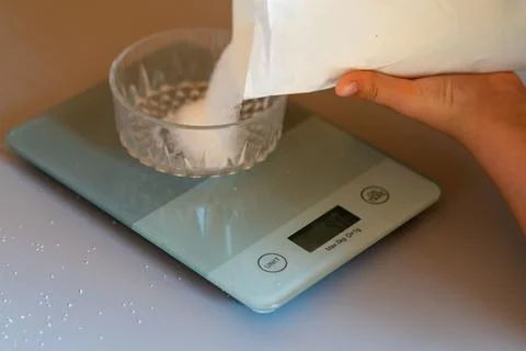 Weighing sugar from a pack on a kitchen scale Stock Photos