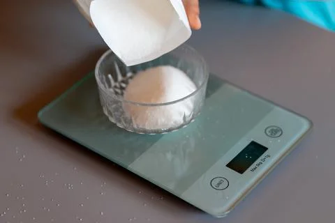 Weighing sugar from a pack on a kitchen scale Foto stock