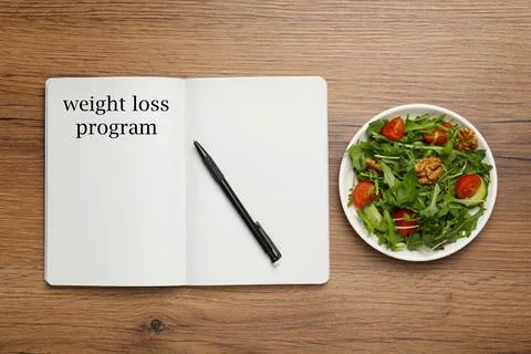 Weight loss concept. Open notebook with pen and bowl of salad on wooden tab.. Foto stock