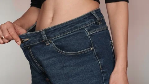 Weight loss progress: indistinguishable belly and waist of a woman in big jeans Stock Footage 306618856