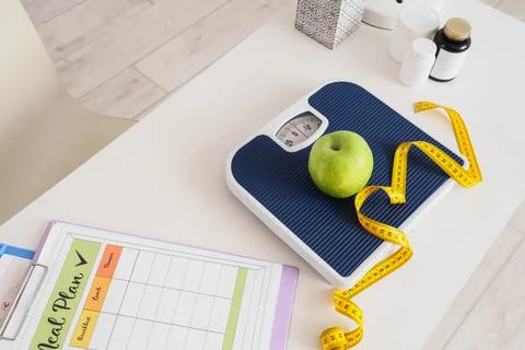 Weight scale with green apple, measuring tape and meal plan Stock Photos