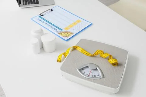 Weight scale with measuring tape and meal planner on white table Stock Photos