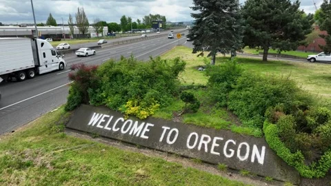 Welcome to Oregon stone border sign with lush green landscaping beside busy Stock Footage 335474773