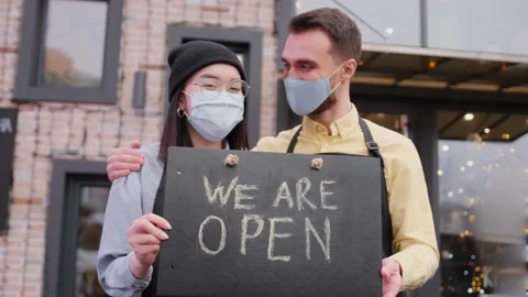 Welcome, we are OPEN. Two friendly waiters wearing protective masks. Multiracial Stock Footage 148242197