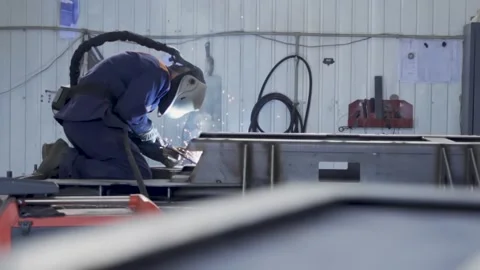 Welder in helmet working on metal structure in factory workshop Stock Footage 314057337