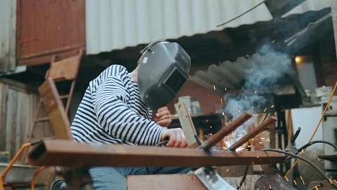 A welder in a mask welds a metal structure in the backyard of the estate. Stock Footage 243514855