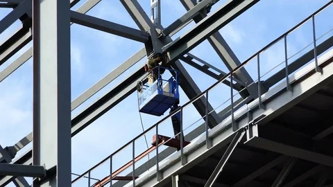 Welder in a mechanical hoist on a platform at a height produces welding work Stock Footage 73814501