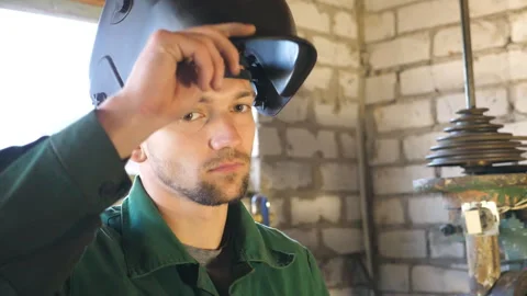 Welder opens mask and looking at camera. Portrait of handsome man with beard Видео 333836800