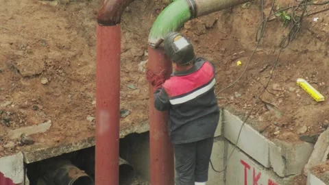 Welder performing powerful arc welding on heating main pipe joint in excavated Stock Footage 344864168