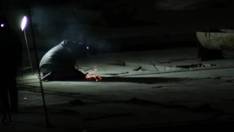 Welder in protective gear performs arc welding in dark industrial workshop at Stock Footage 328818086