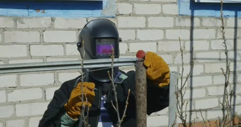 Welder in protective mask and gloves working with welding machine on metal Stock Footage 332738630