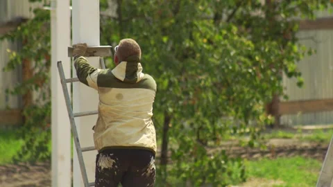 A welder in a protective suit welds metal parts while standing on a ladder at a Stock Footage 307207176