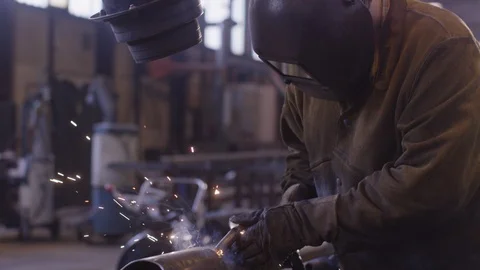 Welder wearing protective gear welding a metal pipe at an industrial site Stock Footage