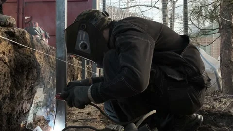 A welder wearing a protective mask makes a support for a fence Stock Footage 233485942
