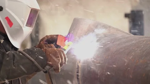 Welder welds pipe. A welder in a protective helmet. Sparks fly out. Snowfall Stock Footage 153291559